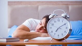 Ein schlafender Mann, im Vordergrund ein Wecker. 