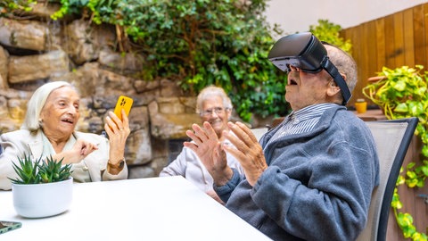 Älterer Mann mit Virtual Reality Brille im Garten eines Pflegeheims.