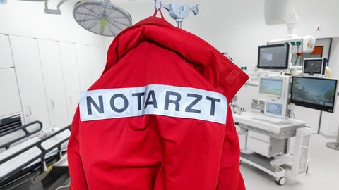 Eine rote Jacke mit der Aufschrift "Notarzt" hängt im Schockraum einer Klinik: Die vom Gesundheitsministerium geplante Reform will Notdienste von Bagatellfällen freihalten und einen Facharzt für Notfallmedizin einführen. Reicht das?