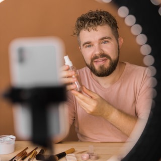 Ein Influencer präsentiert Makeup vor Ringlicht und Smartphone: Auf Instagram, YouTube oder TikTok verbreiten Influencer nicht nur Fotos ihrer Lieblingsessen oder Katzenvideos. Ihre Accounts sind mittlerweile wichtige Verkaufsplattformen geworden. Marken werben mit Follower-starken Accounts für ihre Handtaschen, Sporthosen oder Lippenstift. 