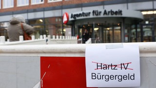 Ein Blatt Papier mit dem Wörtern Harz IV (rot durchkreuzt) und Bürgergeld ist vor einer Baustelle der Agentur für Arbeit zu sehen. Der Bundestag hat für die Einführung des Bürgergelds gestimmt. Es löst 2023 die bisherigen Leistungen von Hartz-IV ab.