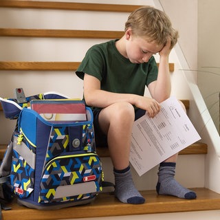 Ein Grundschüler sitzt traurig mit seinem Zeugnis auf der Treppe: Studien zeigen, dass vom Sitzenbleiben niemand profitiert. Dafür sind die Ehrenrunden oft demotivierend und obendrein ganz schön teuer. Einige Bundesländer sind schon ausgestiegen.