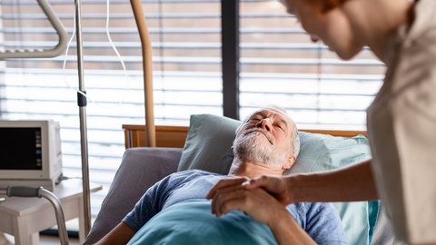 Ein Patient liegt nach einer OP im Bett: Nicht nur ältere Menschen, sondern auch junge oder Säuglinge können nach einer Narkose in einen Zustand des Delirs geraten. Sie sind verwirrt und körperlich unruhig, haben Halluzinationen oder Wahnvorstellungen. Das kann bei Erwachsenen Stunden und Tage nach dem Erwachen auftreten und Tage andauern. Kognitive Beeinträchtigungen können folgen. 