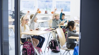 Grundschulkinder beteiligen sich in der Klasse lebhaft am Unterricht: Während die einen die Bewertung durch Noten für motivierend und notwendig halten, finden andere, sie führe in der Schule nur zu kurzfristigem Pauken statt zum nachhaltigen Verstehen. Besser seien individuelle Rückmeldungen statt Ziffernnoten. 