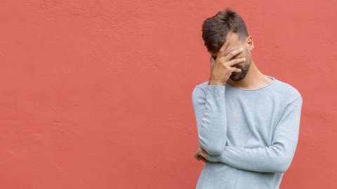 Junger Mann hält sich beschämt die Hand vor den gesenkten Kopf: Psychologinnen und Soziologen sagen, dass die Scham unsere Privatsphäre schützt, zwischenmenschliche Kommunikation regelt und soziale Gruppen stabilisiert. Wer sich schämt, weiß, dass er oder sie sich gegenüber einer anderen Person falsch verhalten hat. Individuelle Schamgrenzen zeigen, wenn uns jemand oder etwas zu nah kommt.