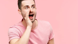 Mann im rosa T-Shirt hält rechte Hand an den Mund und ruft: Die menschliche Stimme ist einzigartig wie ein Fingerabdruck. Studien belegen, dass wir durch den Klang der Stimme Rückschlüsse auf Kompetenz, Attraktivität und Alter einer Person ziehen. 