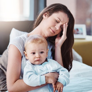 Kopfschmerzen und eine Mutter mit ihrem Baby morgens gemeinsam im Schlafzimmer