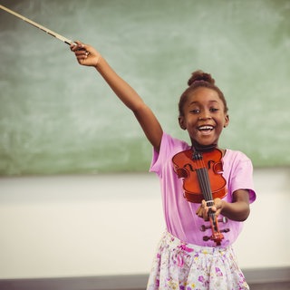 Porträt einer lächelnden Schülerin, die im Klassenzimmer Geige spielt.