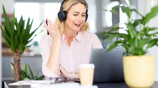 Frau mit Kopfhörern nimmt im Homeoffice an einer Videoschalte teil: Die Pandemie hat das Homeoffice populär gemacht, in Deutschland arbeitet inzwischen jeder Vierte zumindest teilweise von zu Hause. Doch bei den Firmenlenkern ist es umgekehrt: Zwei Drittel wollen ihre Mitarbeiter wieder fünf Tage im Büro sehen. Gefragt sind neue Konzepte für hybrides Arbeiten.