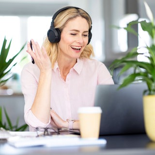 Frau mit Kopfhörern nimmt im Homeoffice an einer Videoschalte teil: Die Pandemie hat das Homeoffice populär gemacht, in Deutschland arbeitet inzwischen jeder Vierte zumindest teilweise von zu Hause. Doch bei den Firmenlenkern ist es umgekehrt: Zwei Drittel wollen ihre Mitarbeiter wieder fünf Tage im Büro sehen. Gefragt sind neue Konzepte für hybrides Arbeiten.