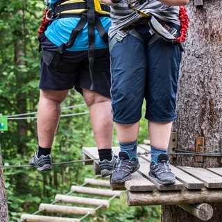 Zwei Jungedliche klettern im Hochseilgarten: In Deutschland gelten rund zwei Millionen Kinder als übergewichtig, 800.000 von ihnen als adipös. Betroffene Kinder und Jugendliche kämpfen aber nicht nur mit ihren Pfunden, sondern auch mit Diskriminierung und Mobbing. Mehr Sportangebote, Ernährungskompetenz, Steuern auf Süßgetränke und Werbeverbote für ungesunde Kinderlebensmittel lauten einige Vorschläge zur Prävention.