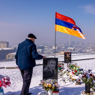 Der 28. Januar ist in Armenien der "Tag der Armee". Auf dem Soldatenfriedhof Jerablur in der Hauptstadt Jerewan besucht 2024 ein Mann an diesem Tag ein blumengeschmücktes Grab und berüht das Bild eines Gefallenen. Daneben weht die Flagge von Bergkarabach. Auf dem Friedhof wurden Soldaten beerdigt, die im Konflikt zwischen Armenien und Aserbaidschan um Bergkarabach starben.