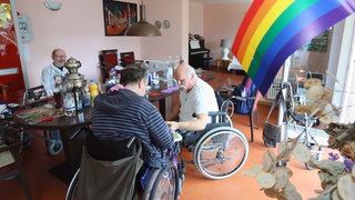 Eine Regenbogen-Fahne schmückt 2015 den Gemeinschaftsraum der Wohngemeinschaft für homosexuelle Senioren in Berlin, die sich zum Mittagessen versammelt haben. Die WG im Berliner "Lebensort Vielfalt" ist eine Pflegeeinrichtungen für Homosexuelle, die sich in herkömmlichen Altenheimen vor Vorurteilen und Diskriminierung fürchten und zurückziehen. Mittlerweile, 2025, gibt es drei Wohnprojekt der Schwulenberatung in Berlin.