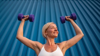 Junge Frau beim Hanteltraining: Da die Muskulatur ab dem 25. Lebensjahr abnimmt, ist Training mit Gewichten wichtig. Vor allem die Muskeln des Fasern-Typ 2, die für Kraft zuständig sind, müssen trainiert werden. Aber auch Ausdauertraining ist notwendig.