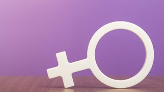 Gender-Symbol einer Frau, liegend vor einem lila Hintergrund:Obwohl Frauen und Männer in Deutschland weitgehend gleichberechtigt sind, wählen viele rollentypische Berufe. Dass Frauen in patriarchalen Ländern viel öfter in "Männerberufe" gehen, ist ein Rätsel. Was hat es mit dem Geschlechter-Paradox auf sich?