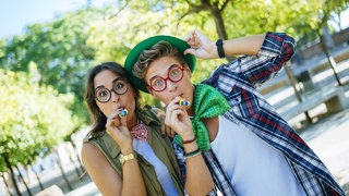 Junges Paar mit Partytröten: Ab 14 strafmündig, ab 16 Bier trinken, ab 18 wählen und als "erwachsen" gelten. Aber ab wann sind wir wirklich erwachsen, und was bedeutet das eigentlich? 