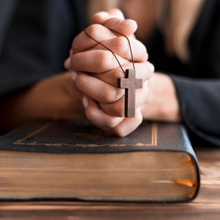 Betende Person mit Kreuz und Bibel: Christlicher Fundamentalismus ist vielschichtig und überkonfessionell. Es gibt Verbindungen zu rechts-konservativen Vertretern der Kirche und des Adels, aber auch zur extremen Rechten. Er ist in großen Teilen antifeministisch, antimuslimisch und antisemitisch. 