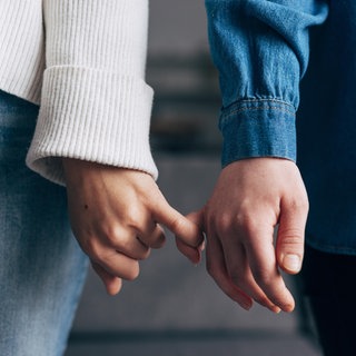 Händer zweier Personen, die die kleinen Finger eingehakt haben: Tastzellen in der Haut reagieren auf Druck oder Temperatur und unterscheiden zwischen bloßem Abtasten und zärtlichen Berührungen. Menschliche Berührungen sind entscheidend für die körperliche und psychische Gesundheit. 