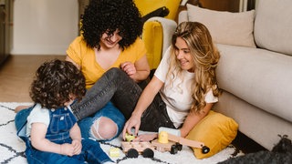 Zwei Mütter spielen mit ihrem Kind: Immer mehr Menschen leben in Patchwork-Familien mit "Bonuskindern", Männer und Frauen ziehen auch ohne Liebesbeziehung zusammen Kinder groß. Die Bundesregierung erarbeitet Vorschläge, um alternative Familienmodelle zu stärken.