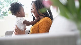 Eine Mutter hält ihr Kind und spielt und spricht mit dem kleinen Mädchen: Die Wörter für die eigene Mutter haben in allen bekannten Sprachen einen "m"-Laut. Die Forschung kennt viele solcher sprachlichen Universalien. Was folgt daraus für die Natur der Sprache und des Sprechens?