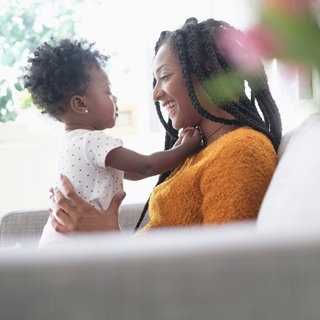 Eine Mutter hält ihr Kind und spielt und spricht mit dem kleinen Mädchen: Die Wörter für die eigene Mutter haben in allen bekannten Sprachen einen "m"-Laut. Die Forschung kennt viele solcher sprachlichen Universalien. Was folgt daraus für die Natur der Sprache und des Sprechens?