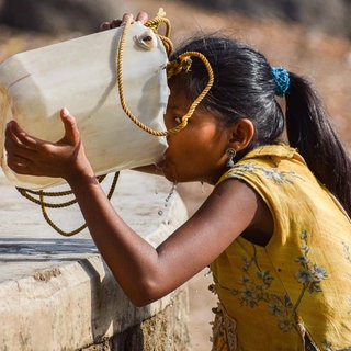 Ein Mädchen in Indien trinkt aus einem Kanister. Der Brunnen ist fast ausgetrocknet: Extremes Wetter wie beispielsweise eine Hitzewelle wirkt sich auf die Gesundheit des Menschen aus. Das Institut für Global Health der Universität Heidelberg untersucht die Folgen von extremem Wetter und entwickelt Präventionsmaßnahmen.