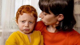 Mutter wendet sich ihrem traurig-wütenden Kind zu: Es gehört zu einer gesunden emotionalen Entwicklung, dass Kinder lernen, ihre Gefühle zu verstehen und auszudrücken und auch die anderer zu respektieren. Mit speziellen Programmen kann das trainiert werden – von Kindern, Jugendlichen und sogar noch Erwachsenen. 