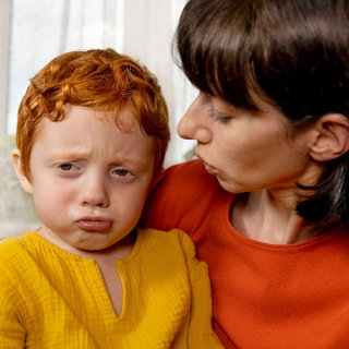 Mutter wendet sich ihrem traurig-wütenden Kind zu: Es gehört zu einer gesunden emotionalen Entwicklung, dass Kinder lernen, ihre Gefühle zu verstehen und auszudrücken und auch die anderer zu respektieren. Mit speziellen Programmen kann das trainiert werden – von Kindern, Jugendlichen und sogar noch Erwachsenen. 