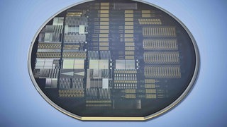 Nahaufnahme eines kreisförmigen photonischen Chips mit komplexen Schaltkreisen. Der dunkle Chip zeigt goldene und silberne mikroskopische Strukturen, die für die Verarbeitung von Photonen optimiert wurden, vor einem hellblauen Hintergrund.