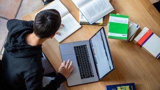 Student arbeitet an einer Hausarbeit mit Laptop und Büchern, tags: KI, ChatGPT, Uni