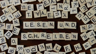 Das Bild zeigt die Wörter "Lesen" und "Schreiben" gelegt aus kleinen Holzbuchstaben.