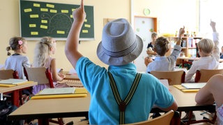 Junge mit Hut und Hosenträgern sitzt in einer Schulklasse: Um sich die Namen vieler neuer Schüler so schnell wie möglich zu merken, können Lehrer zu einem einfachen Trick greifen: Man muss zunächst bei jedem ein besonderes Merkmal ausmachen – eine Brille oder eine abgefahrene Frisur. Dies verknüpft mann dann in Gedanken mit dem Namen. 