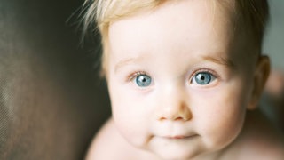 Baby schaut mit neugierigen blauen Augen in die Kamera