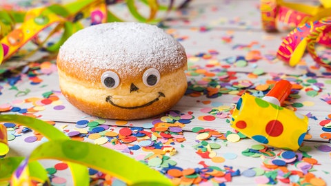 Leckerer Berliner mit niedlichem Gesicht in Faschingsdeko: Feuchter Zucker klebt, weil Zucker und Wasser etwas gemeinsam haben, das sie buchstäblich verbindet: Wasserstoff