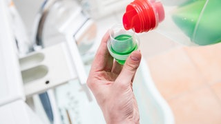 Flüssiges Waschmittel wird eingefüllt: Tenside, Enzyme, Bleichmittel und Mizellen helfen, die Wäsche sauber zu bekommen. Wie genau funktioniert das? Und was hilft gegen welche Flecken?