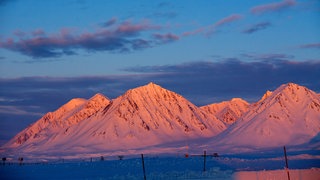 Von der untergehenden Sonne rot angeleuchtet sind die schneebedeckte bis zu 1.000 Meter hohe Berge am 9 April 2015 in der Nähe der Forschungsstation Kings Bay in Ny-Ålesund auf Spitzbergen (Norwegen) zu sehen. Ab dem Polarkreis geht die Sonne an manchen Sommertagen gar nicht mehr unter.