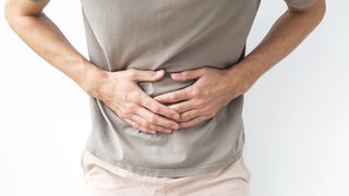 Ein Mann, der sich vor Schmerzen an den Bauch fasst, möglicherweise mit Verdauungsproblemen