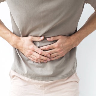 Ein Mann, der sich vor Schmerzen an den Bauch fasst, möglicherweise mit Verdauungsproblemen