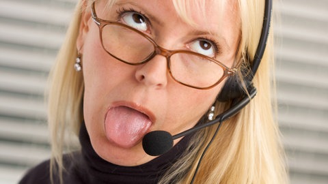 Blonde Frau spricht mit verdrehten Augen genervt in ein Headset: Unsere Gesellschaft misst dem Beruf viel Bedeutung bei: Identität, Anerkennung, Struktur. Was passiert, wenn wir arbeitslos werden oder einen Bullshit-Job als sinnlos empfinden?