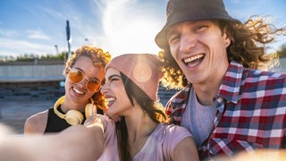 Drei Freunde machen fröhlich ein Selfie im Freien: Mit anderen Menschen auf gleicher Wellenlänge zu sein, fühlt sich gut an. Man kommt schnell ins Gespräch, weiß wie der andere tickt und muss nicht viel erklären: Es vibet eben einfach. 