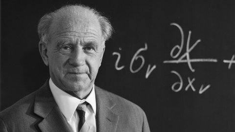 Porträtaufnahme von Werner Heisenberg vor einer Tafel mit physikalischer Gleichung