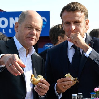 Bundeskanzler Olaf Scholz (SPD) und Frankreichs Präsident Emmanuel Macron (rechts) essen im Oktober 2023 in Blankenese ein Fischbrötchen. Gemeinsames Speisen ist eines der ältesten Instrumente der Diplomatie, um Verständigung und Kooperation zu fördern.