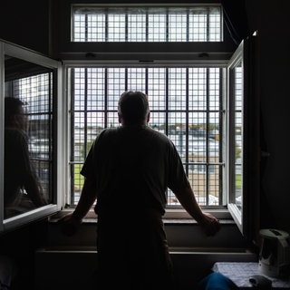 Ein Häftling schaut durch das vergitterte Fenster seiner Zelle: Häftlinge kämpfen mit Süchten, Depressionen, Schuldgefühlen, Ängsten oder Psychosen. Die Suizidrate ist deutlich höher als bei Menschen außerhalb des Strafvollzugs.