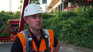 Jochen Reinhard, Ingenieur und Geschäftsführer Schömig-Plan, steht unterhalb einer maroden Brücke. Er trägt einen Schutzhelm und eine Warnweste.