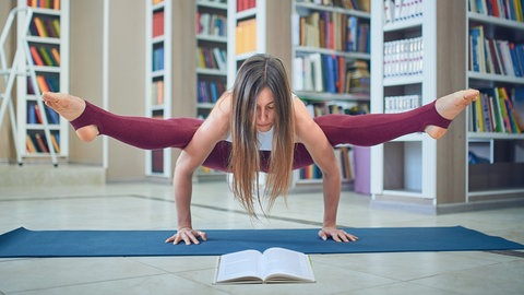 Ein Frau liest ein Buch, während sie im Handstand eine Yoga-Übung macht: Kognitionsforscher haben klar nachgewiesen, dass durch Bewegung die Bildung von Strukturen im Gehirn stimuliert wird. 