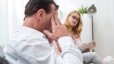 Eine Psychologin im Therapiegespräch mit einem Patienten: Die posttraumatische Belastungsstörung (PTBS) verankert sich nicht nur in der Psyche, sondern auch im Körper Betroffener. Entsprechend vielfältig sind die Therapieformen.