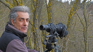 Der Vorsitzende der Gesellschaft zur Erhaltung der Eulen (EGE), Stefan Brücher, steht in einem Wald im Kreis Mayen-Koblenz vor einem Spektiv, einem Beobachtungsfernrohr.