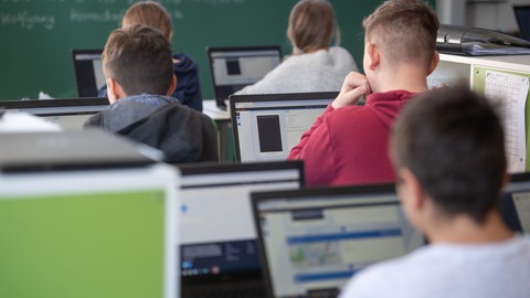 Schülerinnen und Schüler nehmen im Klassenzimmer einer 9. Klasse einer Gemeinschaftsschule mit Hilfe von Laptops und Tablets teil