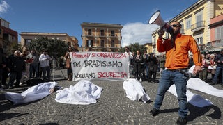 Menschen liegen in Pozzuoli mit Laken bedeckt auf dem Boden. Die Teilhehmer der Demonstration fordern im März 2025 aufgrund des starken Bradyseismos mehr Sicherheit und Kontrollen an Gebäuden in der Region der Phlegräischen Felder.