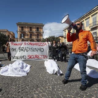 Menschen liegen in Pozzuoli mit Laken bedeckt auf dem Boden. Die Teilhehmer der Demonstration fordern im März 2025 aufgrund des starken Bradyseismos mehr Sicherheit und Kontrollen an Gebäuden in der Region der Phlegräischen Felder.